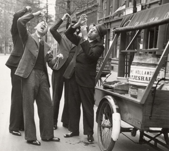 Men eating herring by holding a tail