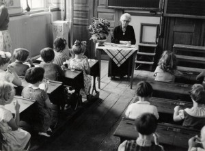 children sitting in a classroom with a female teacher in front