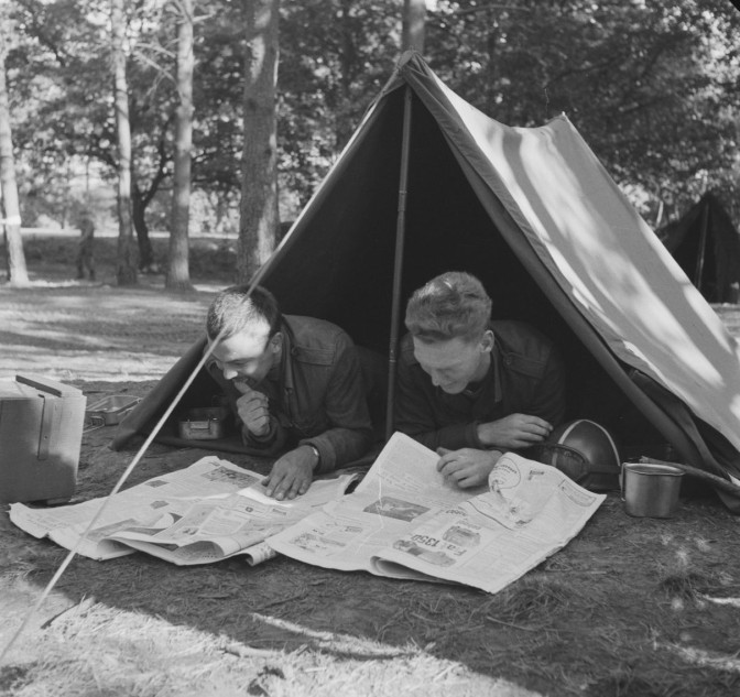 two soldiers reading a newspaper in front of their tents