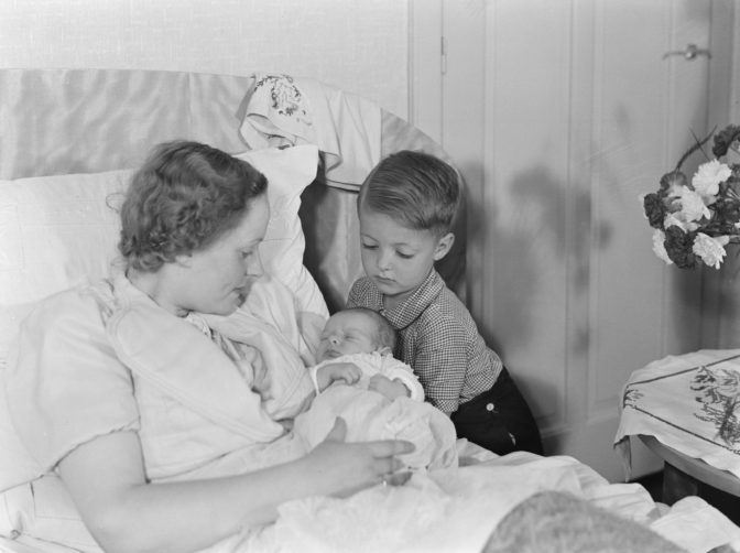 mother in bed with a baby, with the brother looking on