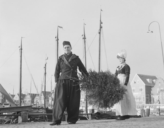 Couple in traditional costume carrying a Christmas tree