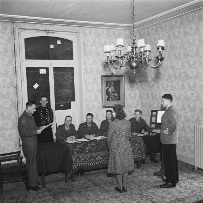 woman standing before a table where several men are seated